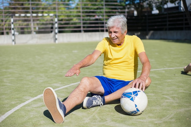 Determined senior man getting ready for match on sunny day. Caucasian man with grey hair in sport clothes warming up on sport field, stretching. Football, sport,  leisure activities concept