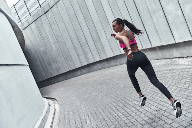 Determined to win. Full length of young woman in sports clothing jogging while exercising outdoors