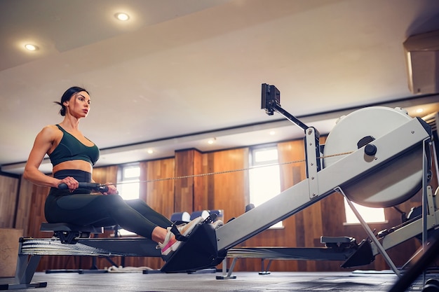 Photo determined young woman working out on row machine in fitness studio