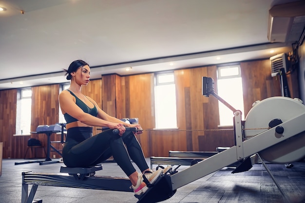 Photo determined young woman working out on row machine in fitness studio