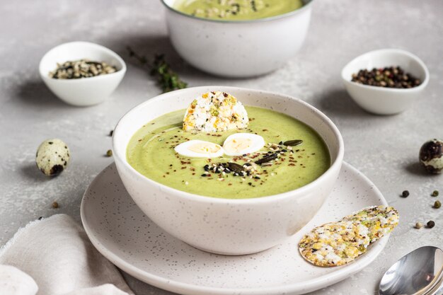 Detox broccoli cream soup with seed mix, quail egg and crackers in bowl 