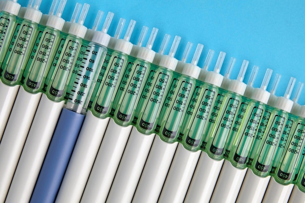 Diabetic insulin pens lined up on a blue background One blue syringe in a row of many gray syringes