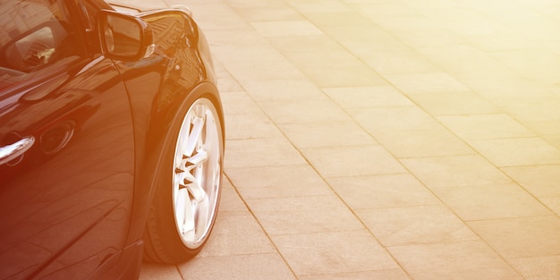 Diagonal view of a black glossy car with white wheels, which stands on a square of gray tiles