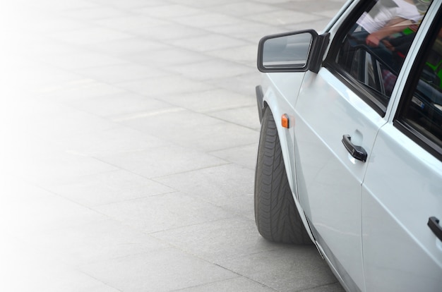 Diagonal view of a white glossy car that stands on a square of gray tiles