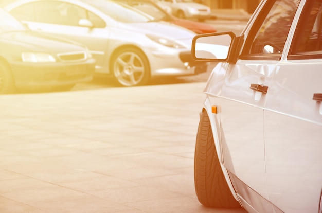 Diagonal view of a white glossy car that stands on a square of gray tiles