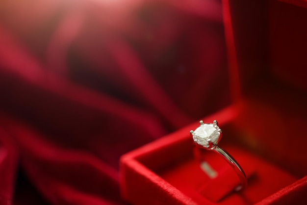 Diamond ring in jewelry gift box on red fabric background