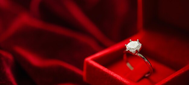 Diamond ring in jewelry gift box on red fabric background