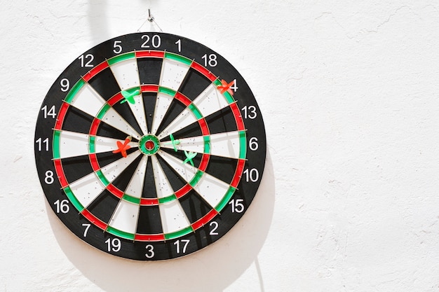 Diana with its green and red nailed darts, hanging on the white wall illuminated by the sun.