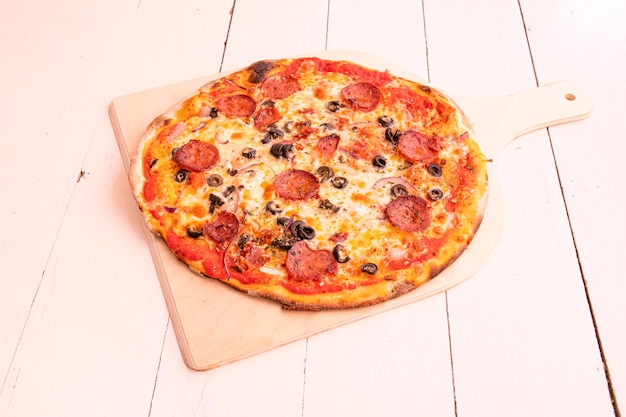 Diavola pizza with black olives plenty of mozzarella cheese red onion and spicy pepperoni on wooden board