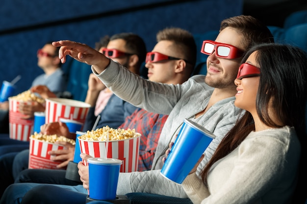 Did you see it? Handsome young man pointing with his hand showing something on the cinema screen to his female friend