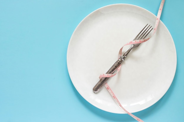 Diet concept. Fork on a white plate with centimeter. 