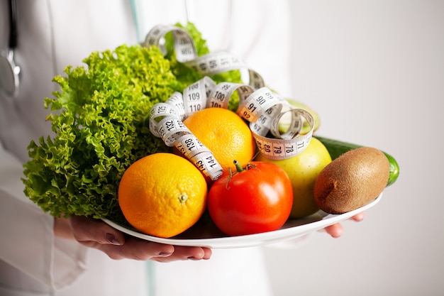 Diet concept, nutritionist holding a full plate of fresh fruit with measuring tape