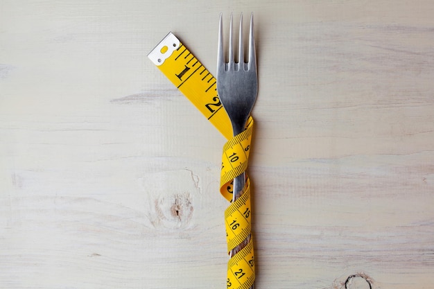 Photo diet light wooden background fork wrapped in a meter fork on white background