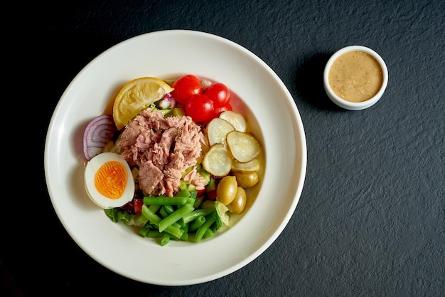 Diet nicoise salad with tuna, egg and asparagus in a white plate on a black background