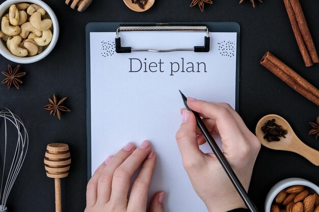 DIET PLAN Baking cooking Ingredients on black background. Top view. Blank clipboard copy space. Home baking: cookies, bread, cake. Cinnamon sticks, nuts spices eggs flour