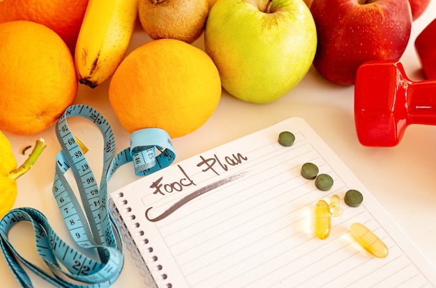 Photo diet plan, menu or program, weight loss, measuring tape, dumbbells and dietary food fresh fruit on a white table