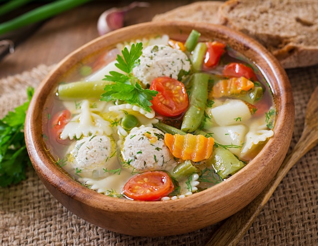 Diet vegetable soup with chicken meatballs and fresh herbs in wooden bowl