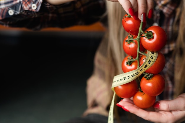 Diet weightloss and fitness organic natural food products for healthy eating woman holding fresh tomatoes with twisted measuring tape in hand