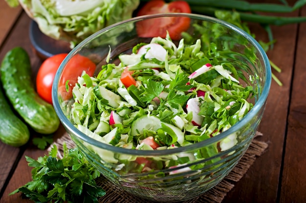 Dietary healthy salad of fresh vegetables in a glass bowl on a wooden table.