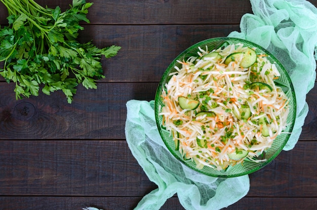 Dietary salad with cabbage, cucumber, carrot, greens. Juicy spring salad with fresh vegetables on a wooden table. Proper nutrition. Top view.