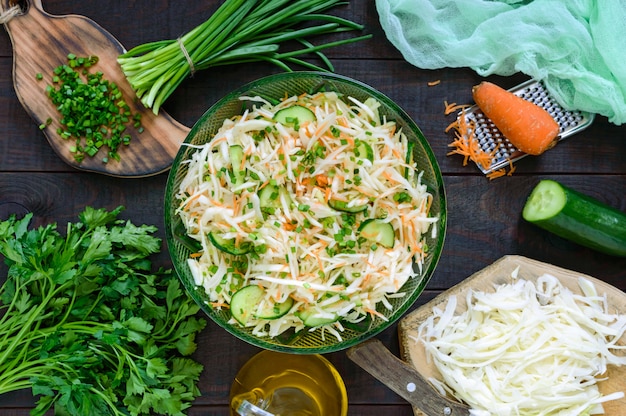 Dietary salad with cabbage, cucumber, carrot, greens. Juicy spring salad with fresh vegetables on a wooden table. Proper nutrition. Top view.