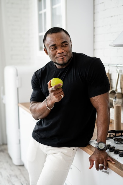 Dieting concept Handsome young multiracial man standing in the kitchen with healthy food and eating apple Fruits and vegetables