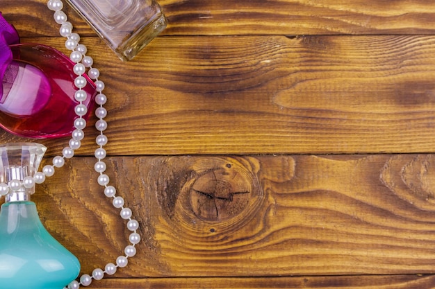 Different bottles of perfume and pearl necklace on wooden background Top view copy space