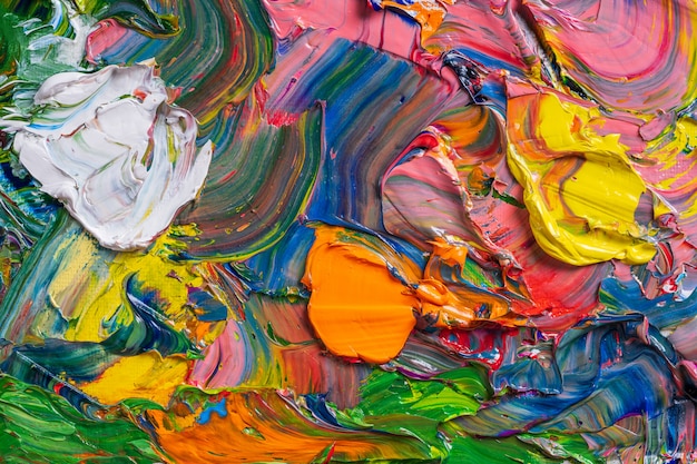 Different bright colors of oil paints are mixed on a palette close-up.