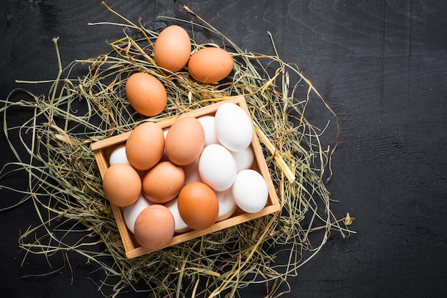 Different chicken eggs in wooden box on black background. Copy space