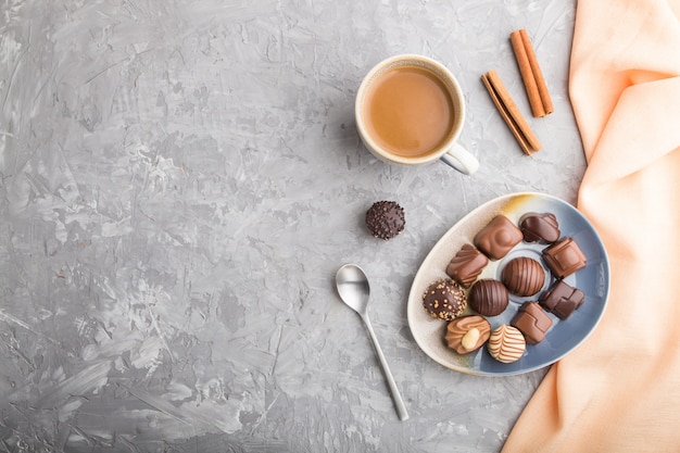 Different chocolate candies and a cup of coffee on a gray concrete background. top view, copy space.