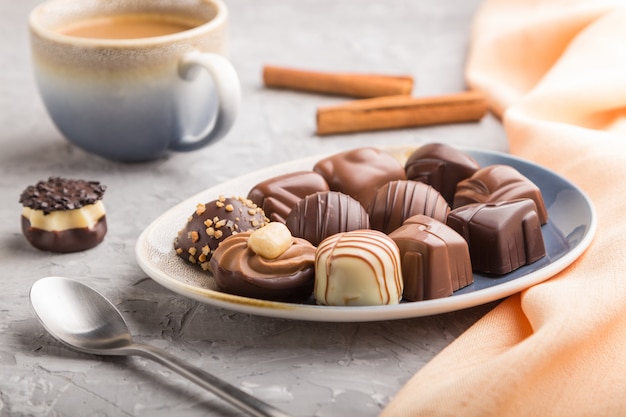 Different chocolate candies and a cup of coffee on a gray concrete surface. side view, selective focus.