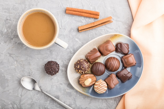 Different chocolate candies and a cup of coffee on a gray concrete surface. top view, close up.