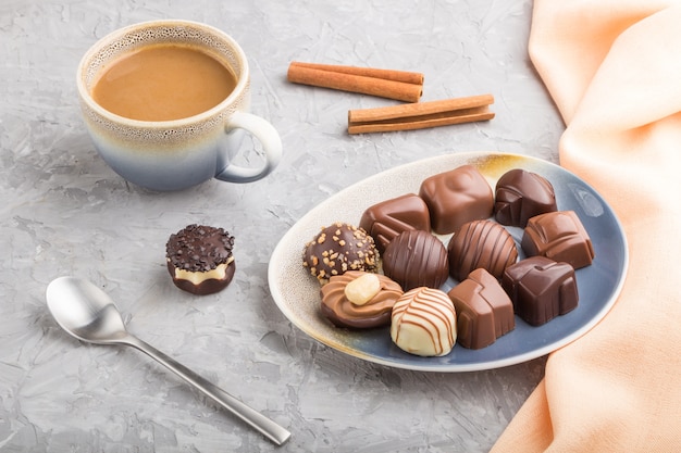 Different chocolate candies and a cup of coffee on a gray concrete table. side view, close up