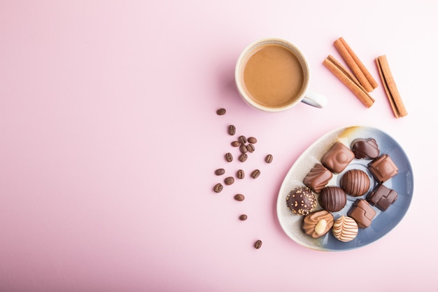 Different chocolate candies and a cup of coffee on a pink pastel background. top view, copy space.