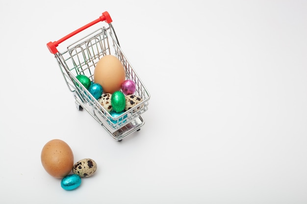 Different color and size eggs are in the grocery cart on the white background