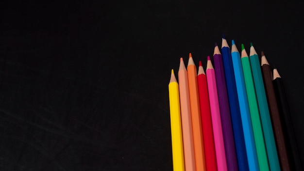 Different color wooden pencils on black chalkboard background