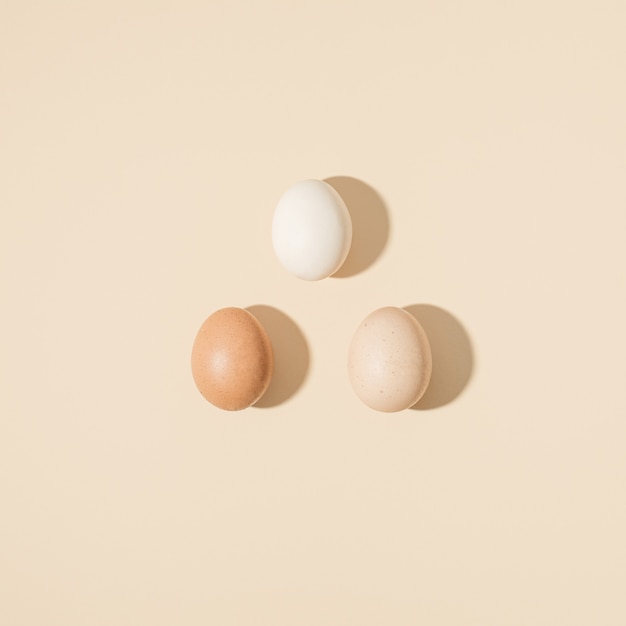 Different colored eggs on pastel beige background. Minimal food concept, creative pattern.