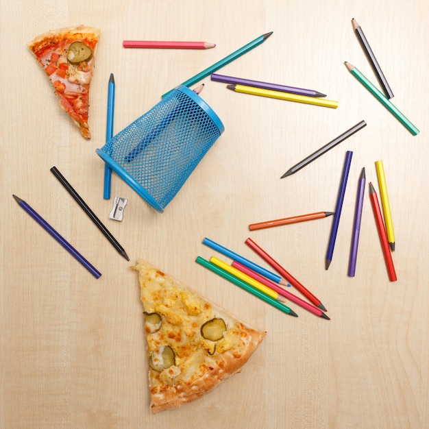 Different colored wooden pencils with metal holder sharpener and two pieces of pizza