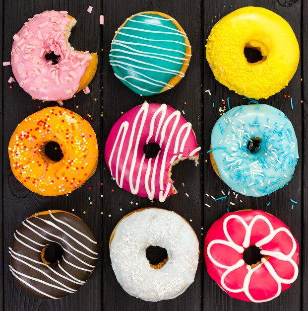 Different colorful donuts on black wooden background