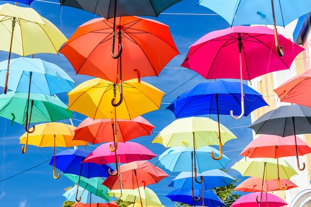 Different colorful umbrellas hanging over the street against blue sky