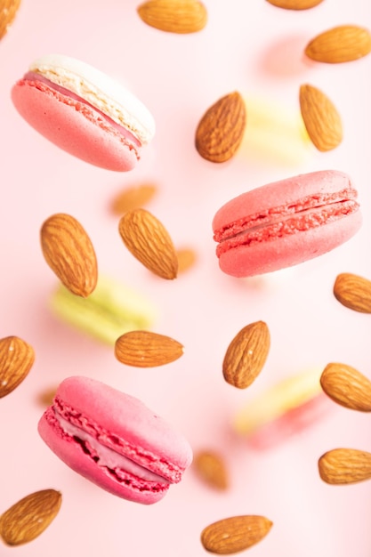 Different colors flying macaroons and almonds frozen in the air on blurred pink background top view close up