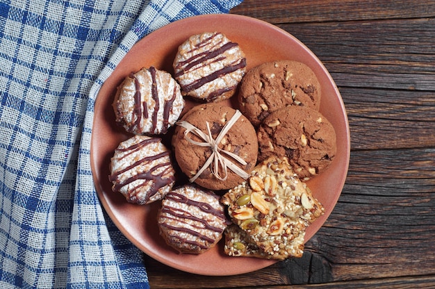 Different cookies in a plate on rustic wooden table with blue tablecloth, top view