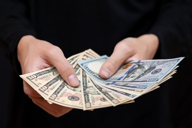 Different dollar bills in the hands of a young man in dark clothes, close-up.