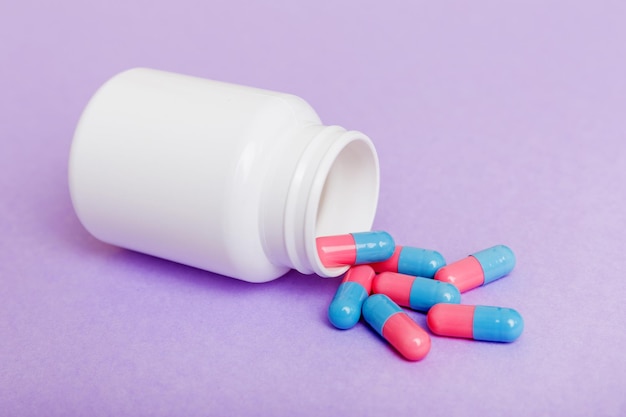 Different drugs and health supplement pills poured from a medicine bottle health care and medical top view on colored background