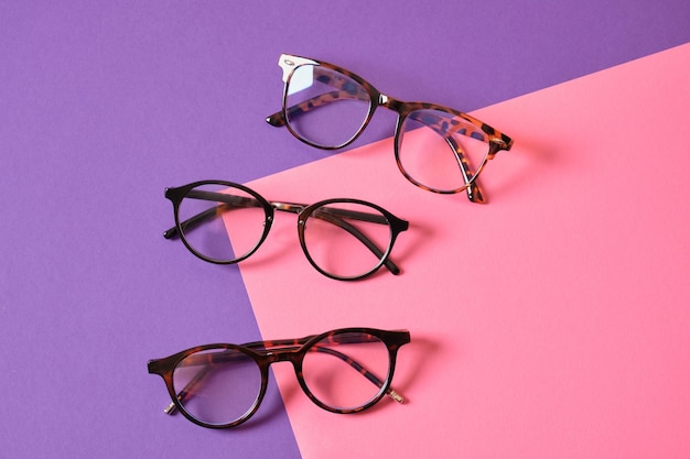 Different fashion eye glasses on pink and purple geometric background, trendy eyeglasses frames copy space