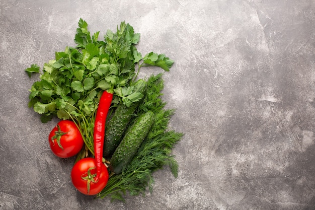 Different fresh greens, tomatos, cucumber and chili on gray concrete. Top view.