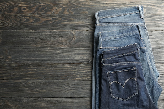 Different jeans folded on a wooden background, space for text