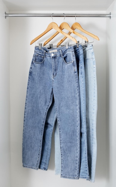 Different jeans hang on wooden hangers in white dressing room Shopping and storage of clothes concep