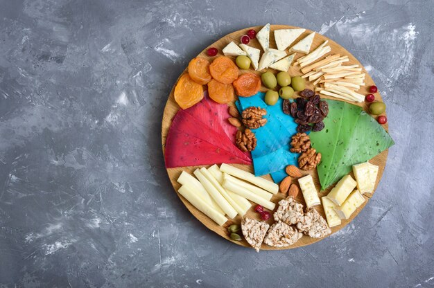 Photo different kinds of cheeses, dried apricots, whole-grain breads, nuts, olives, capers on a wooden board. cheese board, snacks. top view