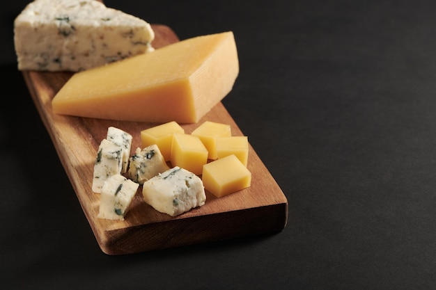 Different kinds of delicious cheese on wooden cutting board Stilllife Set of cheeses dor blu parmesan Black background with copy space